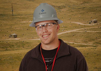 An image of a cameco employee in front of a field wearing a hard hat