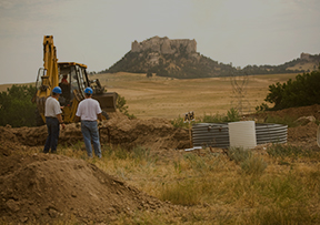 An image of two employees standing near a backhoe in a field