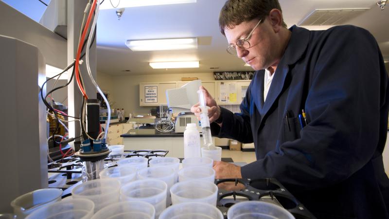 Person in lab coat injecting liquid into plastic container