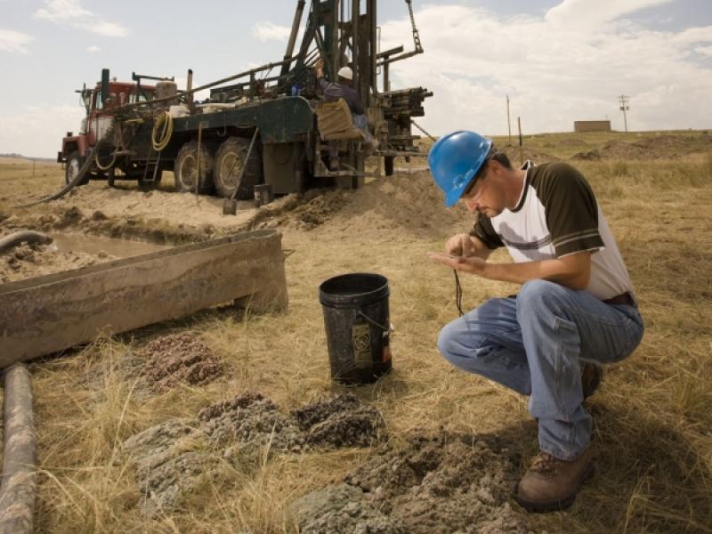 Person in hardhat crouched beside crane inspecting sample